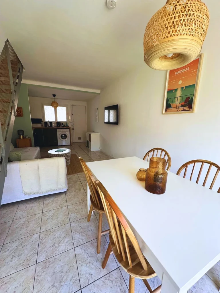 Table à manger blanche et chaises en rotin, cuisine en arrière-plan, projet Gouffé par Maison Solthée, architecte d'intérieur à Marseille