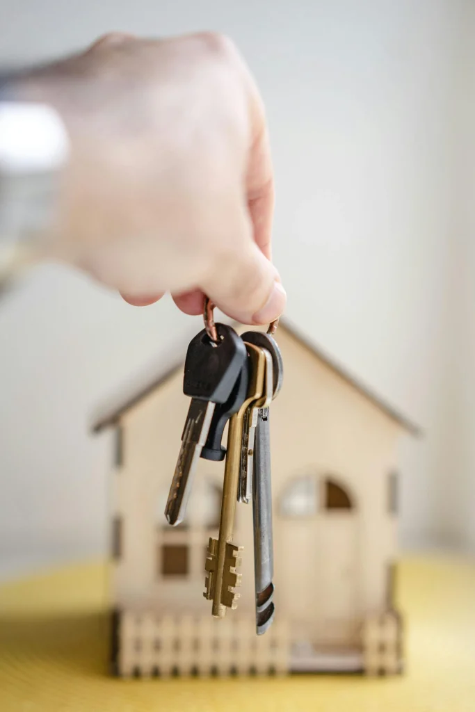 Main tenant un trousseau de clés devant une petite maison en bois