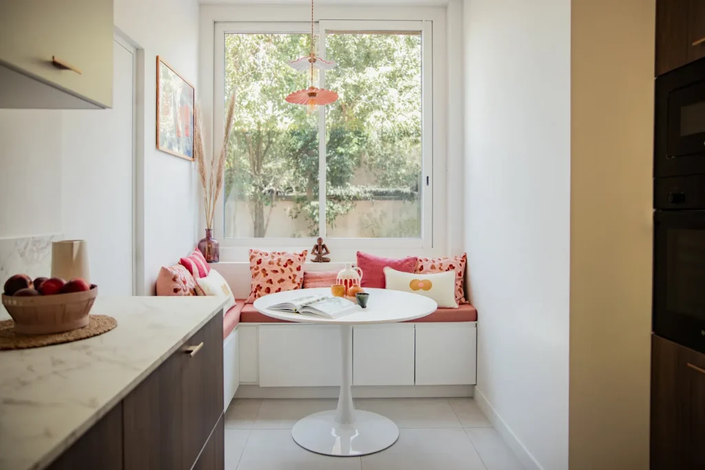 Coin repas avec banquette sous la fenêtre, coussins roses et table ronde, projet Barnabé par Maison Solthée, architecte d'intérieur à Marseille