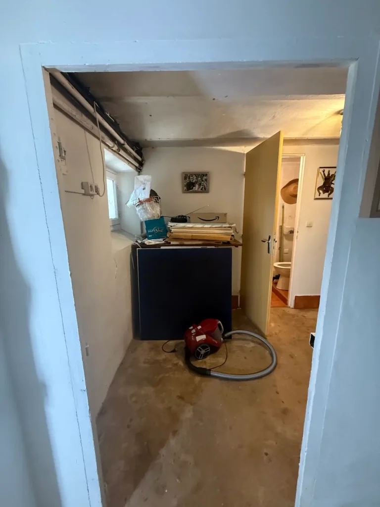 Avant travaux : petite pièce sous plafond bas, sol brut, porte ouverte sur des toilettes, projet Augustine par Maison Solthée, architecte d'intérieur à Cassis