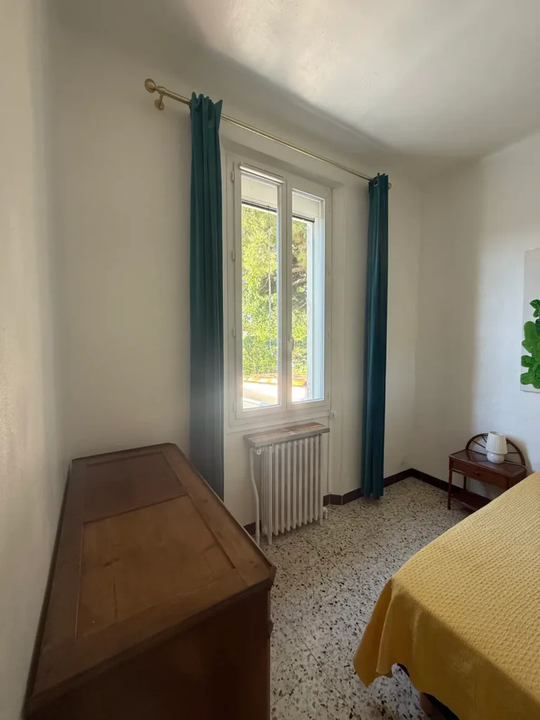 Avant travaux : chambre avec fenêtre, rideaux bleus, commode et sol moucheté, projet Augustine par Maison Solthée, architecte d'intérieur à Cassis