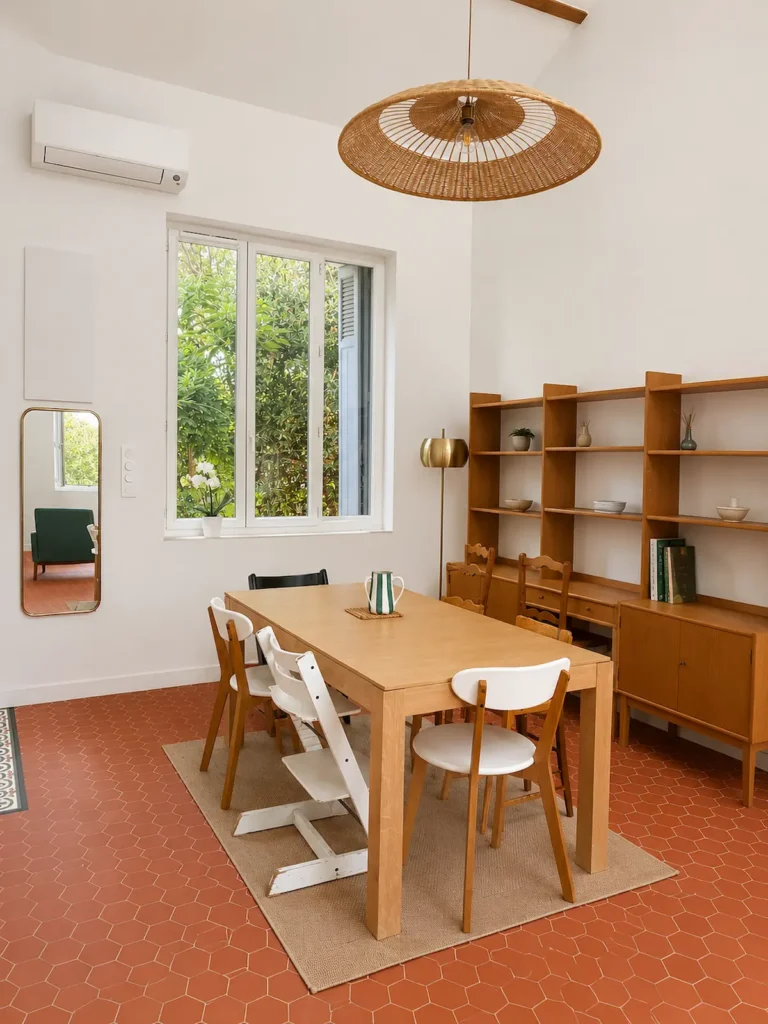 Salle à manger avec table en bois clair, buffet vintage, suspension en rotin et sol terracotta, projet Augustine par Maison Solthée, architecte d'intérieur à Cassis